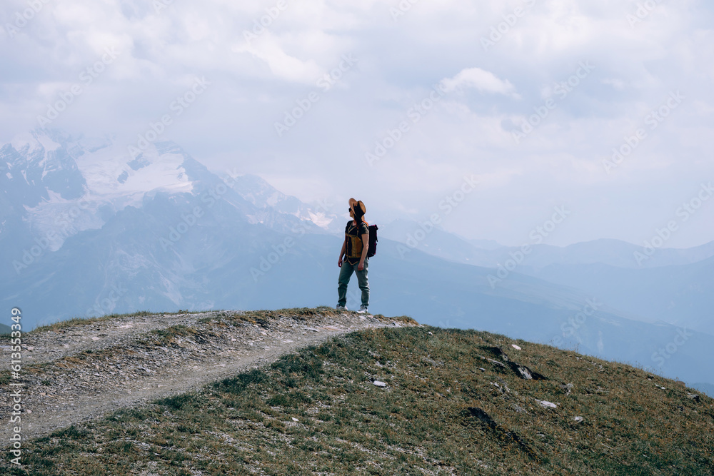 Fototapeta premium Woman in wide sun hat and backpack, tourist on hiking route to Koruldi Lakes, Svaneti region, Mestia Georgia. The concept of travel and active recreation. Summer day