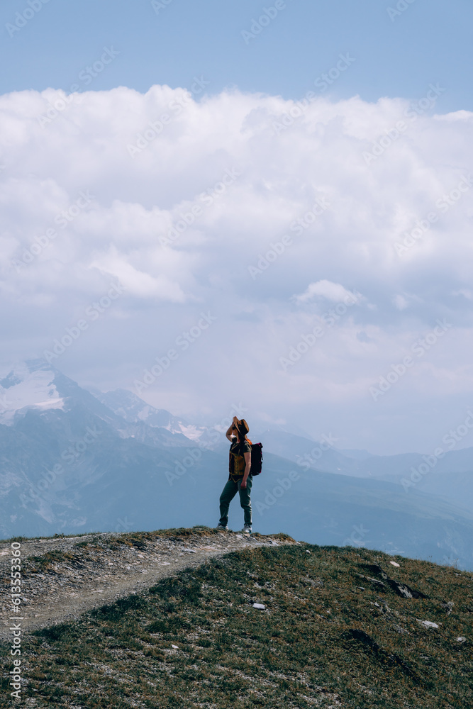 Fototapeta premium Woman in wide sun hat and backpack, tourist on hiking route to Koruldi Lakes, Svaneti region, Mestia Georgia. The concept of travel and active recreation. Summer day. Vertical photo