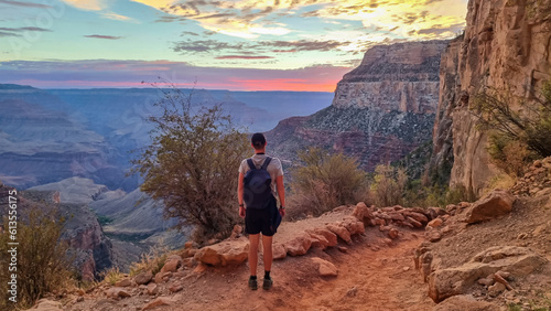 Rear view of man with backpack hiking along Bright Angel trail with panoramic aerial overlook of South Rim of Grand Canyon National Park, Arizona, USA, America. Amazing vista after sunrise in summer