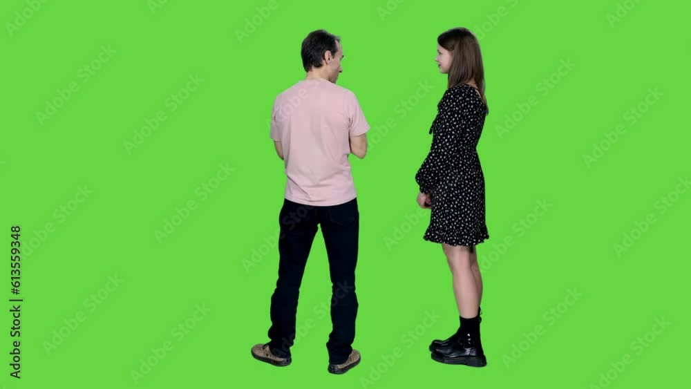 Back view adult man in casual wear explains something and shows to young woman in polka-dot dress on green background, Chroma key Back view adult man in casual wear explains something and shows to young woman in polka-dot dress on green background, Chroma key