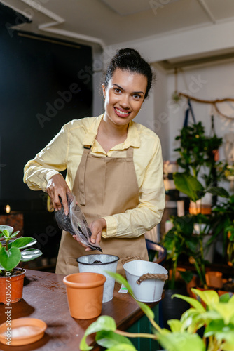 Vertical shot of plant store female french worker wearing apron filling pot with the soil. Seedlings planting process. Home gardening. Hobbies and leisure concept.