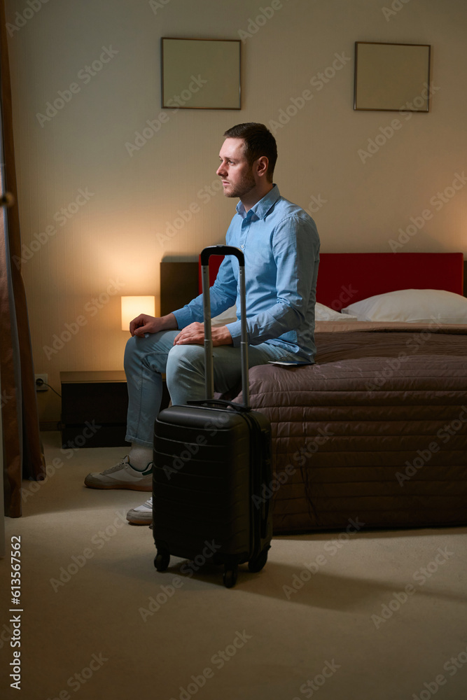 Man looking out window sitting on bed in hotel room