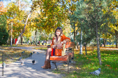 Woman smiling, feeding pigeons in a city central park on warm autumn day. photo