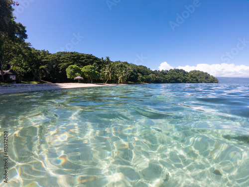 Sun reflecting on clear ocean water with sandy beach in background at Waitatavi Bay