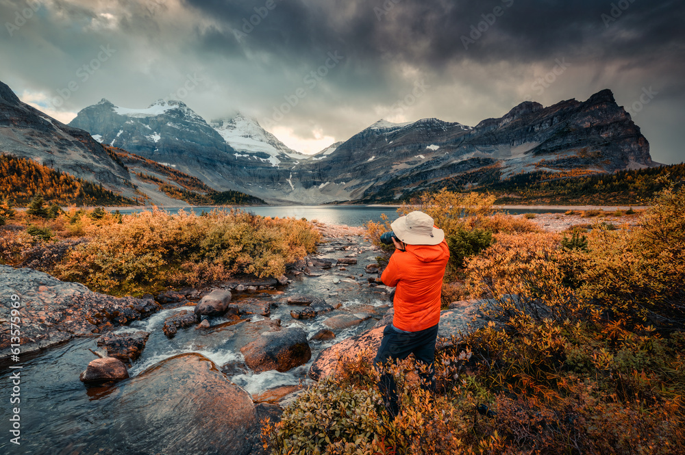 Travel photographer man taking a photo with camera at mount assiniboine in autumn wilderness by lake magog on moody day