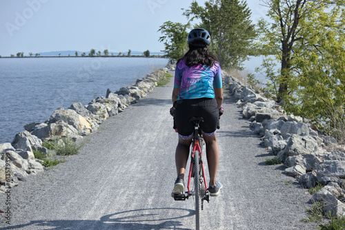 woman riding bike on gravel trail (young south asian, indian rider on bicycle trail) burlington vermont colchester causeway path (brown skin, athletic clothes, cycling jersey, biking shorts, helmet) photo