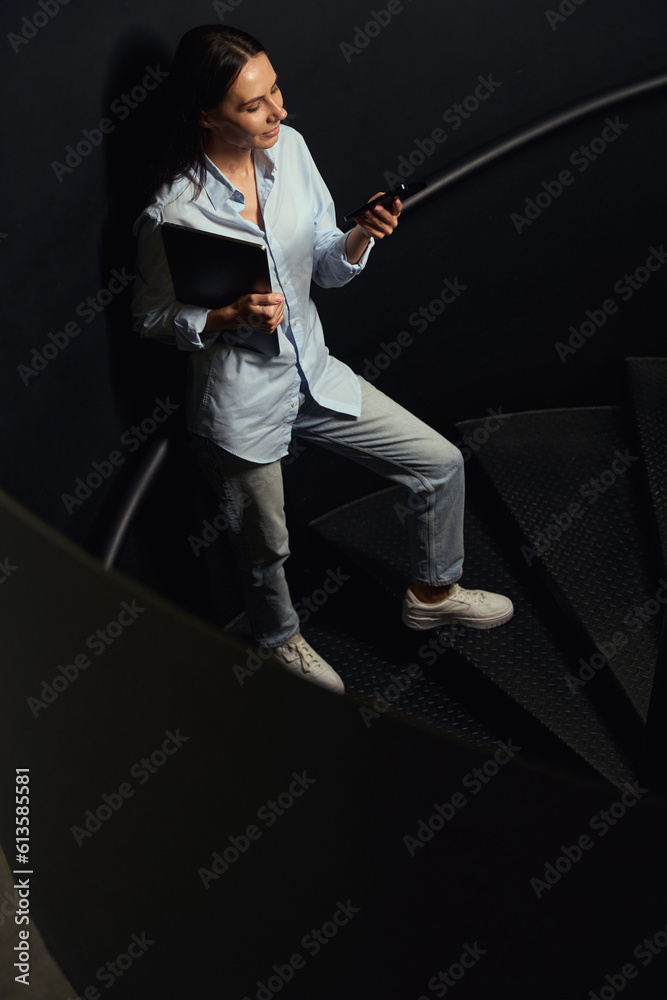 Female freelancer reading something on mobile phone on spiral staircase