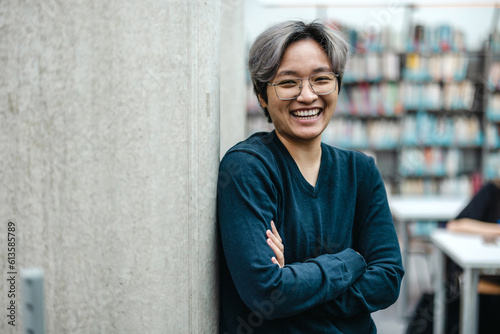 Bilde på lerret Portrait of smiling asian student standing with arms crossed in college library