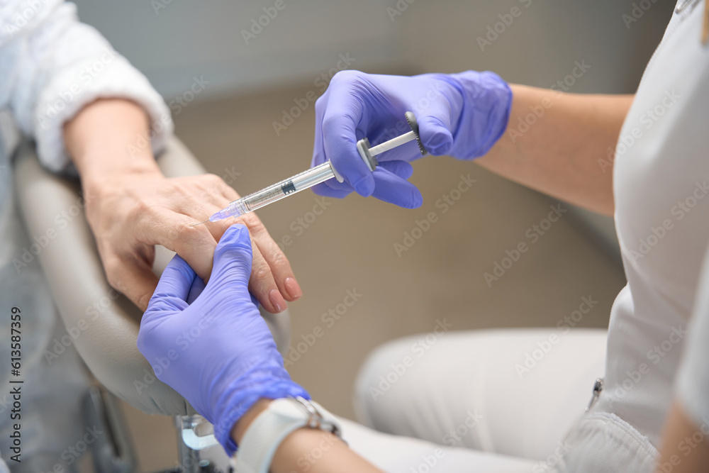 Closeup of beautycian hands in gloves making knuckle injection Closeup of beautycian hands in gloves making knuckle injection