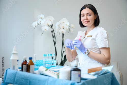 Happy female medical beautician in gloves holding package with syringe