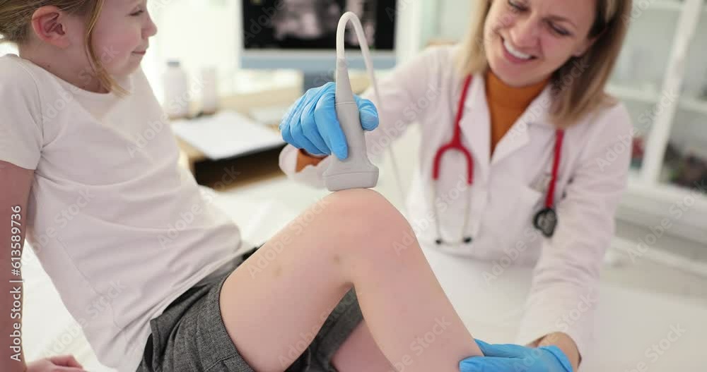 A smiling doctor makes the girl an ultrasound of the knee, a close-up. Diagnosis of injury in a child