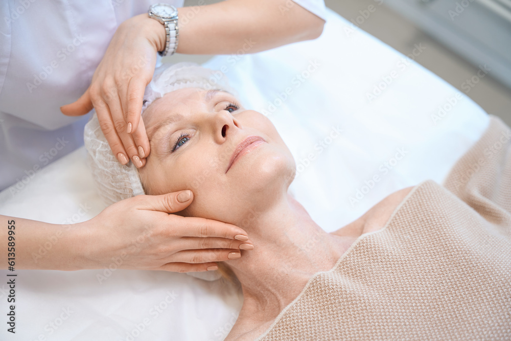 Top view of mature woman in cosmetic cap getting face massage