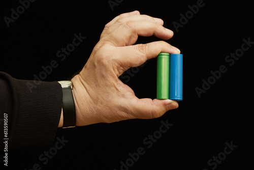 Two batteries between fingers in hand blue and green close-up on dark background