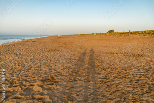 shadows of two persons at the sndy beach with blue sky