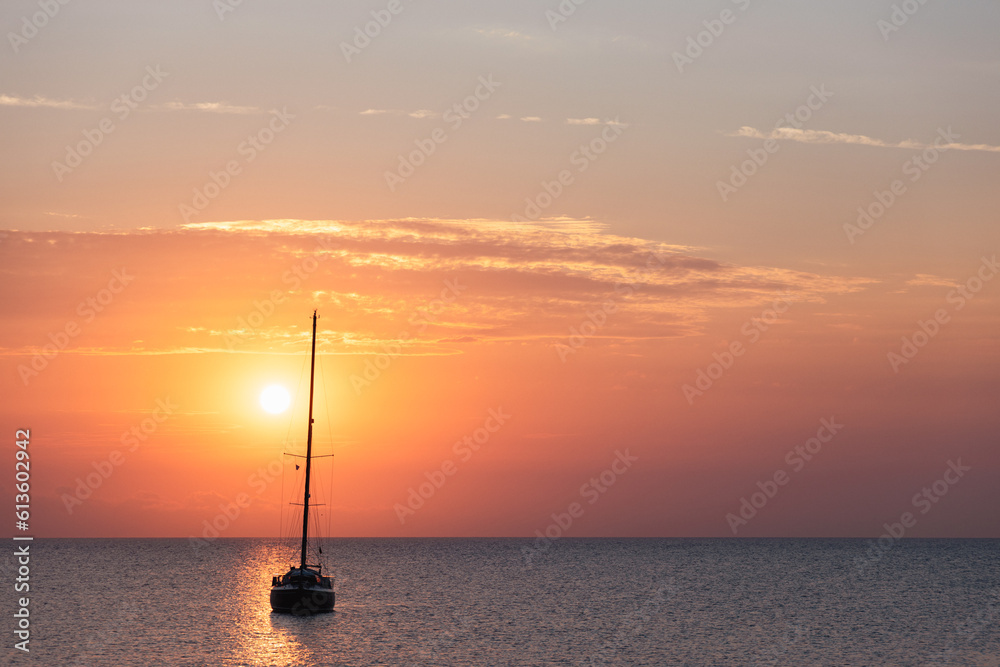Aegean sea sunrise behind calm ocean and silhouette of sailing boat