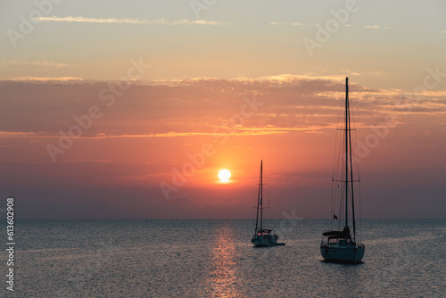 Aegean sea sunrise behind calm ocean and silhouette of sailing boat