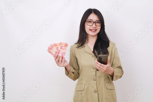 Cute young teacher holding Indonesian banknotes and cell phone while looking at the camera photo