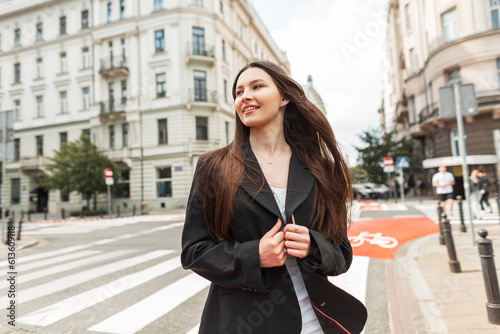 Fashion happy pretty young woman with smile in casual street outfit with white blazer and white dress walks in the city