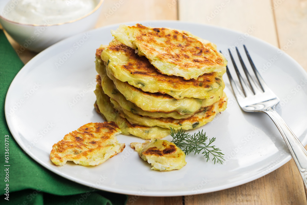Stack of zucchini fritters in plate and cream sauce. Dish on green napkin. Healthy vegan diet food on wooden background. Stack of zucchini fritters in plate and cream sauce. Dish on green napkin. Healthy vegan diet food on wooden background.