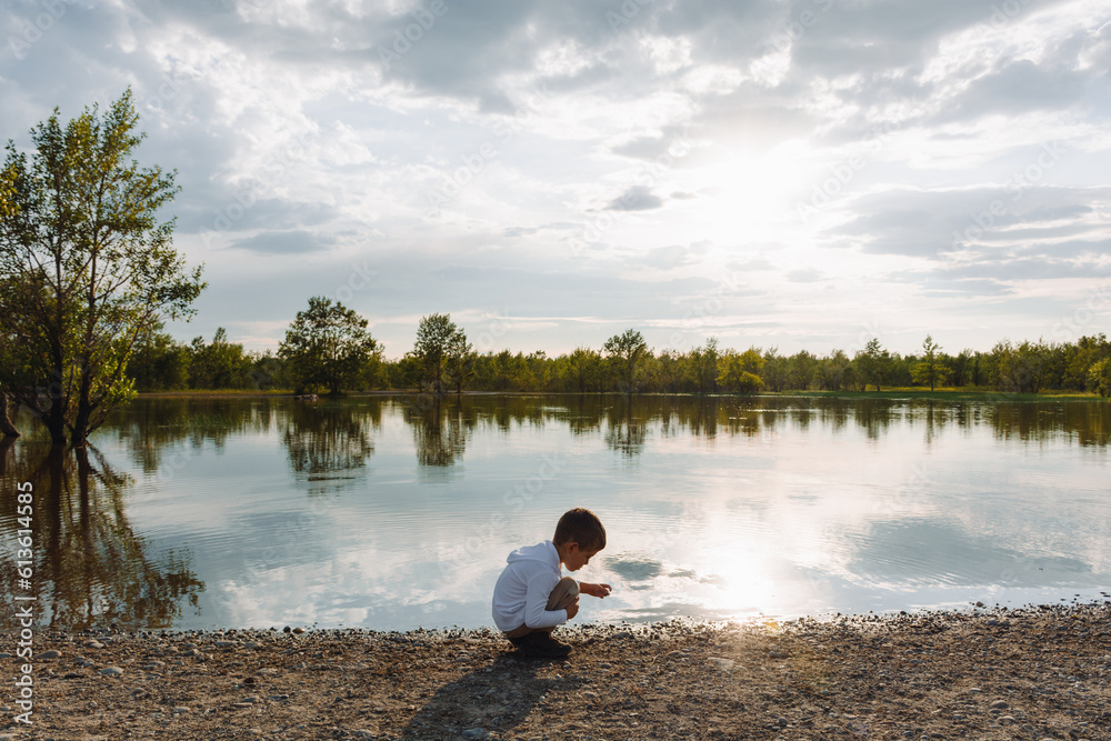 Little boy playing by a pond in a park at sunset