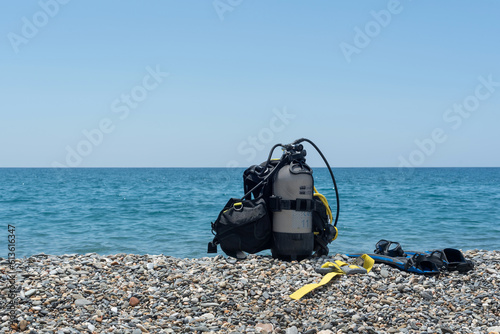 Diving equipment, including oxygen tank, fins, goggles, regulator and weights on the shore of a rocky beach. Water sports. Initiation to scuba diving photo