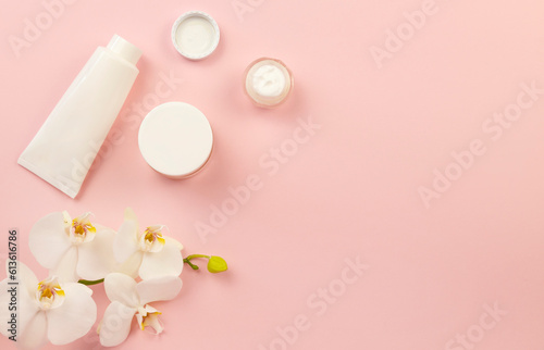 White jars for cosmetic products and orchid flowers on a pink background. Mockup for cosmetic products with place for text.