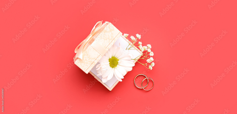 Box with flowers and wedding rings on red background, top view Box with flowers and wedding rings on red background, top view