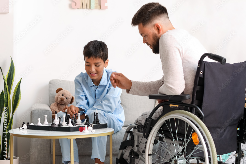 Little boy and his father in wheelchair playing chess at home Little boy and his father in wheelchair playing chess at home