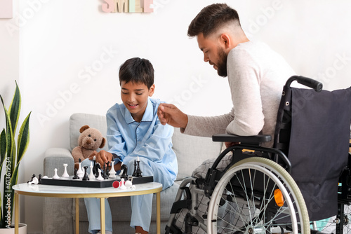 Little boy and his father in wheelchair playing chess at home