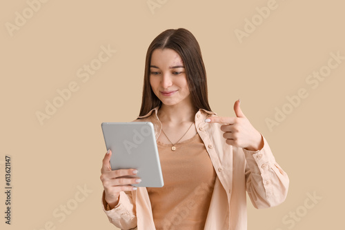 Young woman pointing at tablet computer on beige background