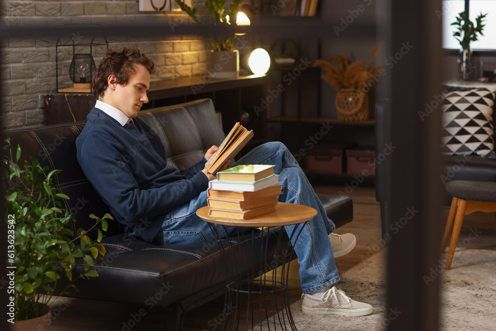 Young man reading book on sofa at home late in evening Young man reading book on sofa at home late in evening