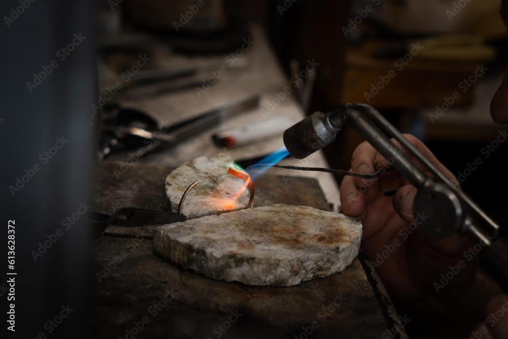 Jeweler soldering on work bench a gold ring bracelet with flame from welding torch in an authentic jewelry workshop Jeweler soldering on work bench a gold ring bracelet with flame from welding torch in an authentic jewelry workshop