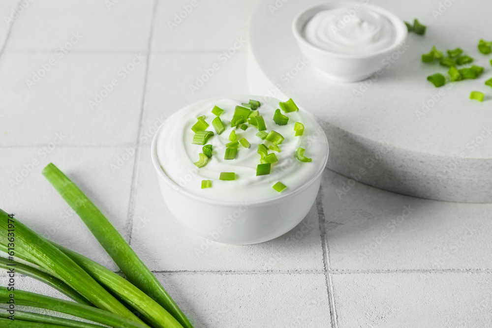Bowl with sour cream and sliced green onion on white tile table