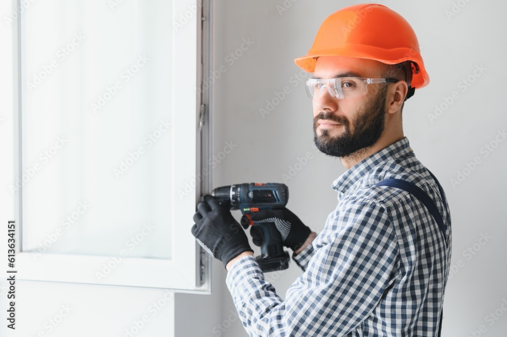 Workman in overalls installing or adjusting plastic windows in the living room at home Workman in overalls installing or adjusting plastic windows in the living room at home