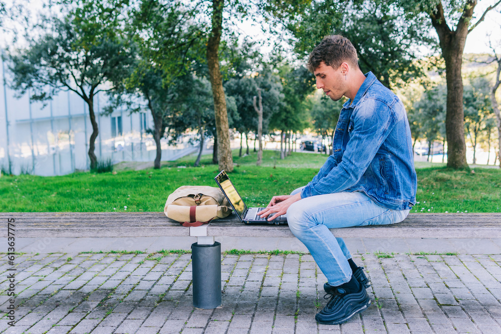 Obraz premium Profile of a young man working with a laptop outdoors