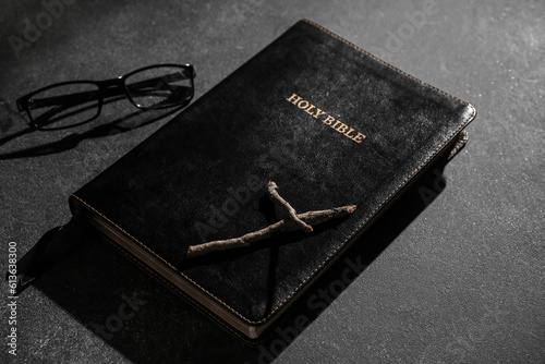 Holy Bible with wooden cross and eyeglasses on black background