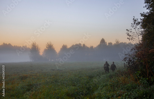 Fotografija Morning autumn landscape with hunters walking in the fog along the edge of the forest