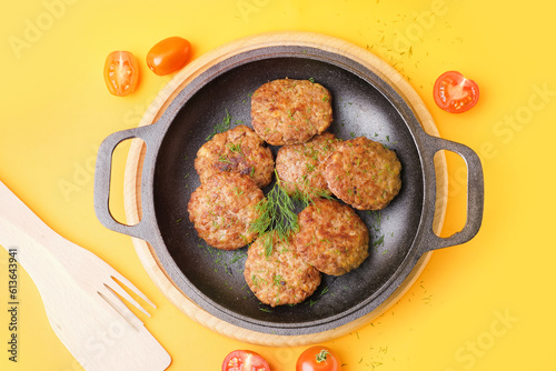 Frying pan with cutlets, dill and tomatoes on yellow background