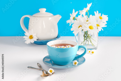 Fototapeta Naklejka Na Ścianę i Meble -  Teapot with cup of natural chamomile tea and flowers on white table near blue wall