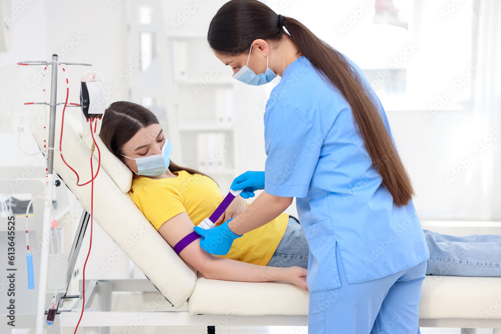 Female nurse preparing young donor for blood transfusion in clinic Female nurse preparing young donor for blood transfusion in clinic