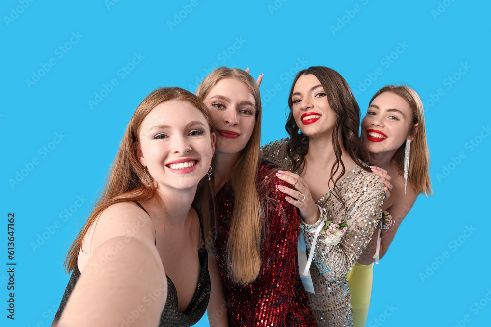Fototapeta premium Young women dressed for prom taking selfie on blue background