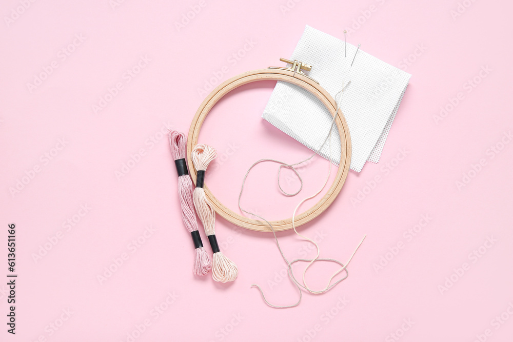 Wooden embroidery hoop with mouline threads, pins and canvas on pink background Wooden embroidery hoop with mouline threads, pins and canvas on pink background
