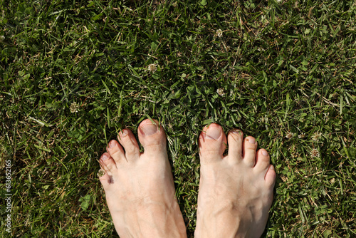 Barefoot on fresh bright green grass on hot day. Male feet stand on lawn outdoors. Freedom, summer relax concept. Earth Day. Earthing or grounded yoga. Rustic lifestyle. Top view. © Andriy Medvediuk