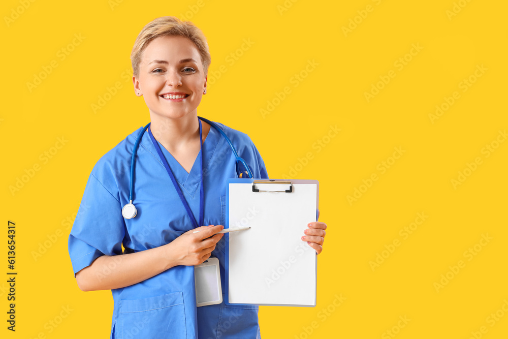 Female medical intern pointing at clipboard on yellow background