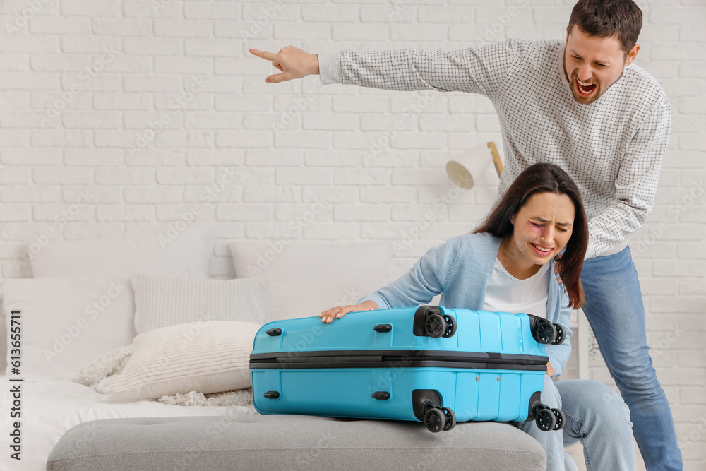 Angry husband kicking his wife with suitcase out in bedroom. Domestic