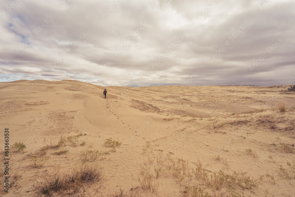Lone man walking under the clouds across the sand at Great Sandhills Ecological Reserve Lone man walking under the clouds across the sand at Great Sandhills Ecological Reserve