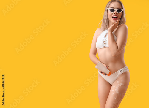 Young woman with sun made of sunscreen cream on her leg against yellow background