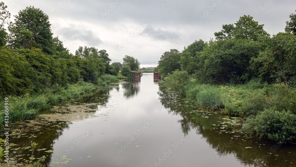 The landscape of the Lithuanian canal, in the distance you can see the metal water gate, it is an ancient metal sluice