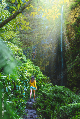 Tourist woman walking along fern overgrown hiking trail torwards picturesque, overgrown waterfall in the Madeiran rainforest. Levada of Caldeirão Verde, Madeira Island, Portugal, Europe. photo