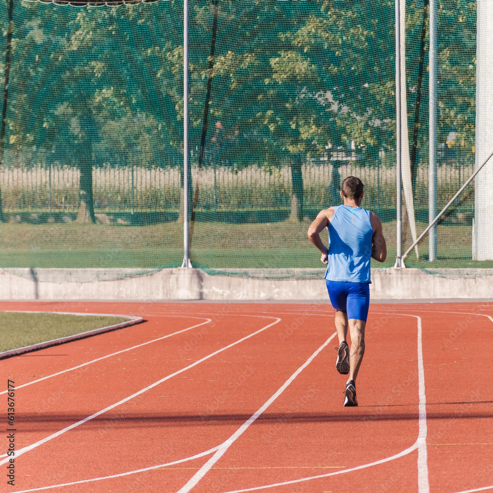 Caucasian male athlete in blue sportswear running alone along an athletic track on the stadium